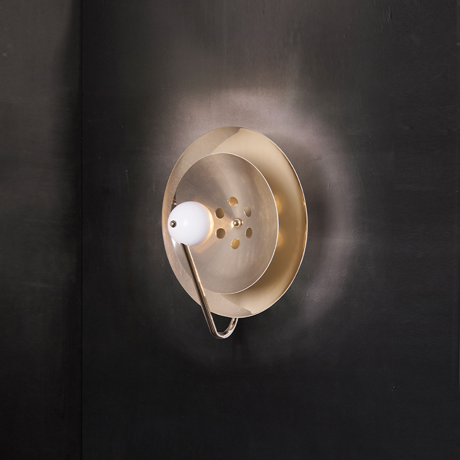 Basie wall light fixture is a modern representation of the sci-fi aesthetics of the 1960s. The vintage mid-century lamp has a set of distinctive features which make it a stunning statement piece. It is an indoor wall light handmade in brass, with a center shade made in Aluminium and a mesmerizing gold-plated standard finish. The lamp shade is lacquered a glossy white for a more modern look.